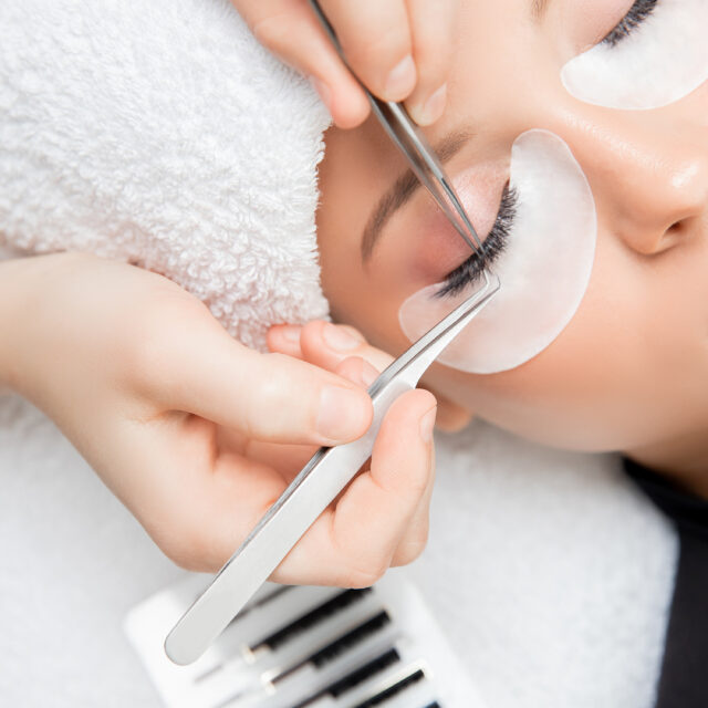 Eyelash extension procedure. Master tweezers fake long lashes beautiful female eyes.