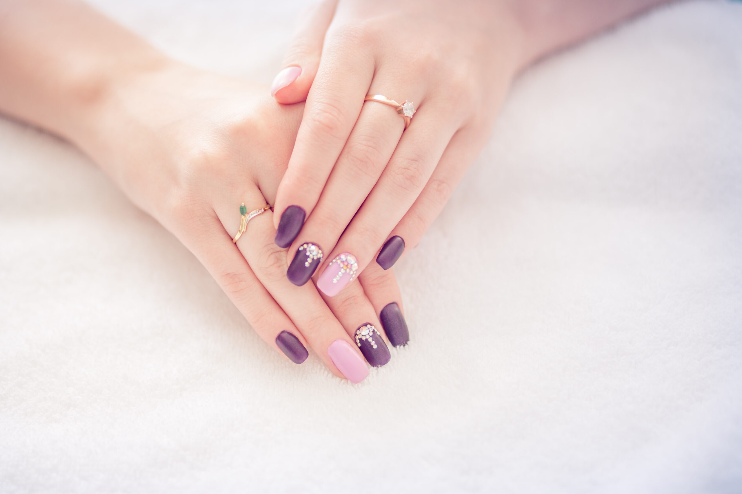 Beautiful colored beige burgundy red pastel colors nail polish with gem crystal stones on hand, closeup. Nail art manicure concept