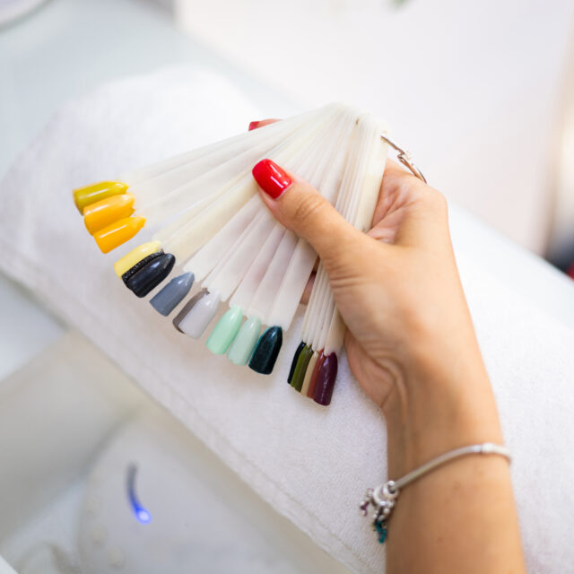 Detail of a hand of an unrecognizable woman chooses the color of the nails from a color palette in a beauty center. Nail manicure. Enamel. Choose new nail color in beauty salon.