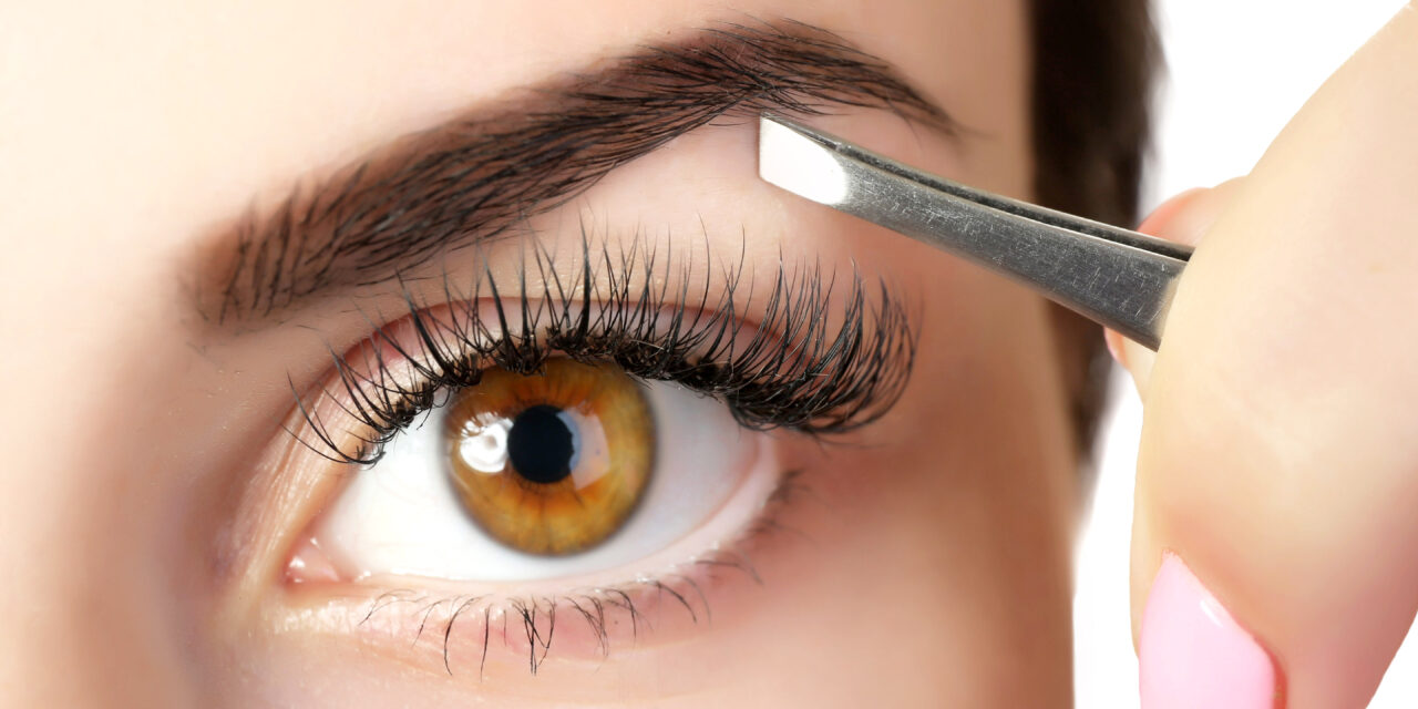 Young woman plucking eyebrows with tweezers close up