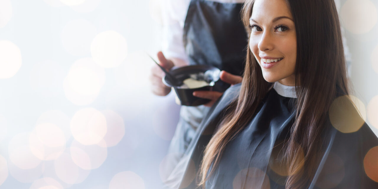 beauty and people concept - happy young woman with hairdresser coloring hair at salon